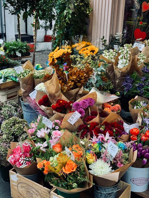 A vibrant display of fresh floral bouquets arranged in paper wrapping, featuring a variety of colorful flowers including pink lilies, orange roses, purple chrysanthemums, white daisies, and red carnat